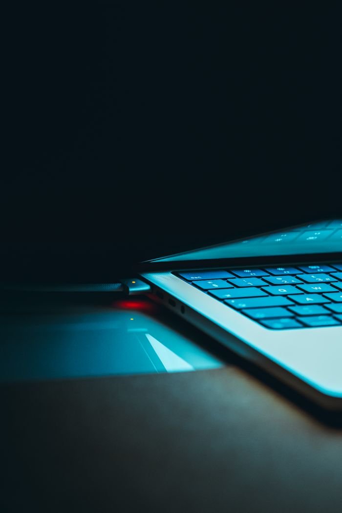 Close-up of a glowing laptop keyboard and lid in a dark setting, highlighting technology and design.